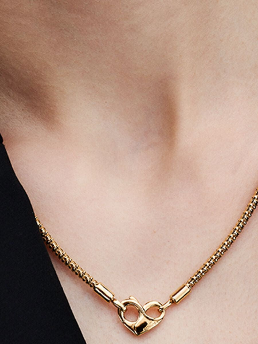 Gold necklace with a heart clasp on a person's neck against a neutral background